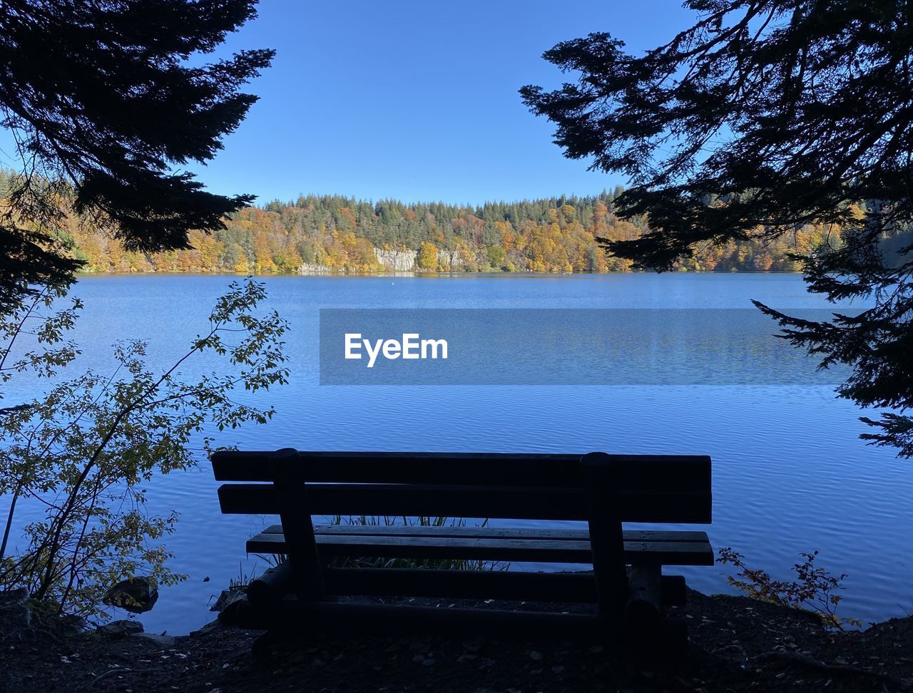 EMPTY BENCH BY LAKE AGAINST BLUE SKY