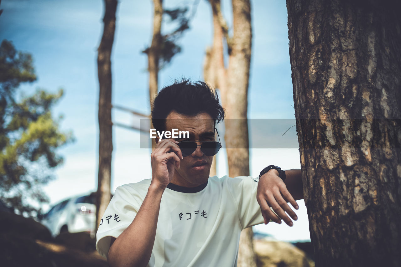 PORTRAIT OF MAN STANDING BY TREE TRUNK