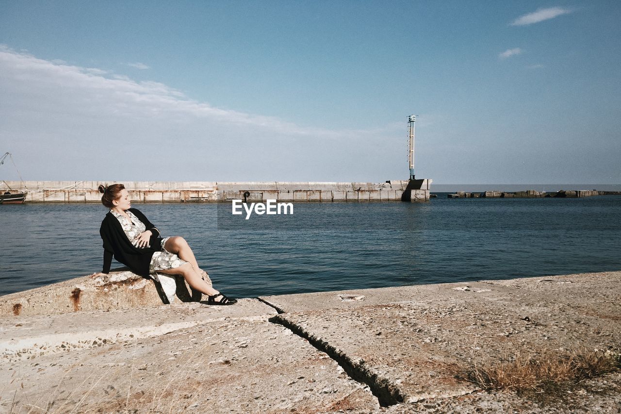 Full length of woman sitting at promenade against sky