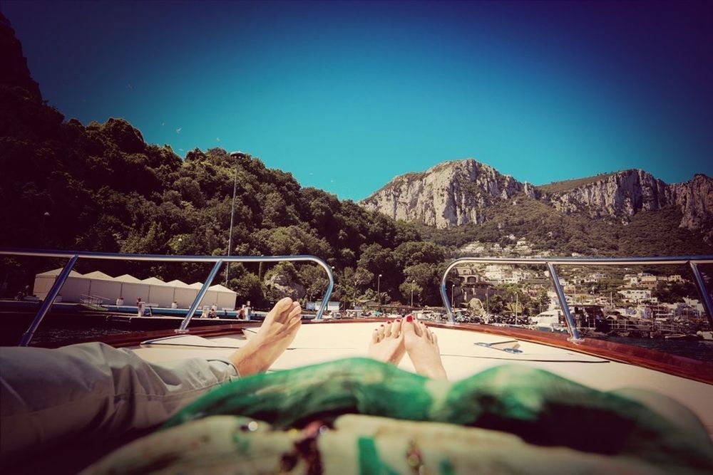 Low section of people on boat against mountains and clear sky