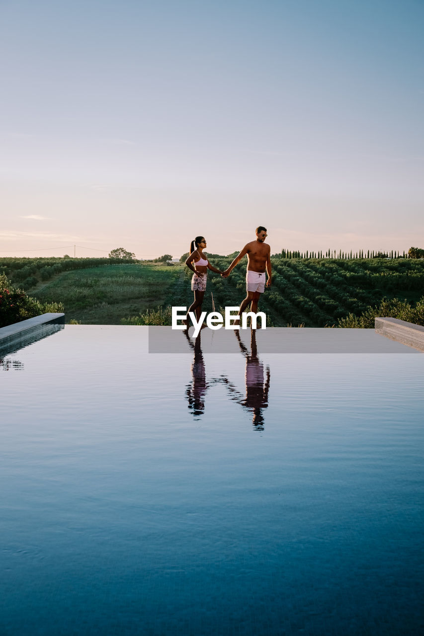 Couple standing by swimming pool in lake against sky