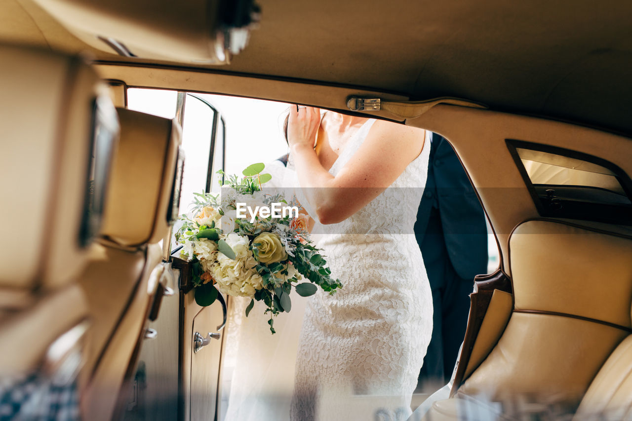 Midsection of bride with bouquet standing by car