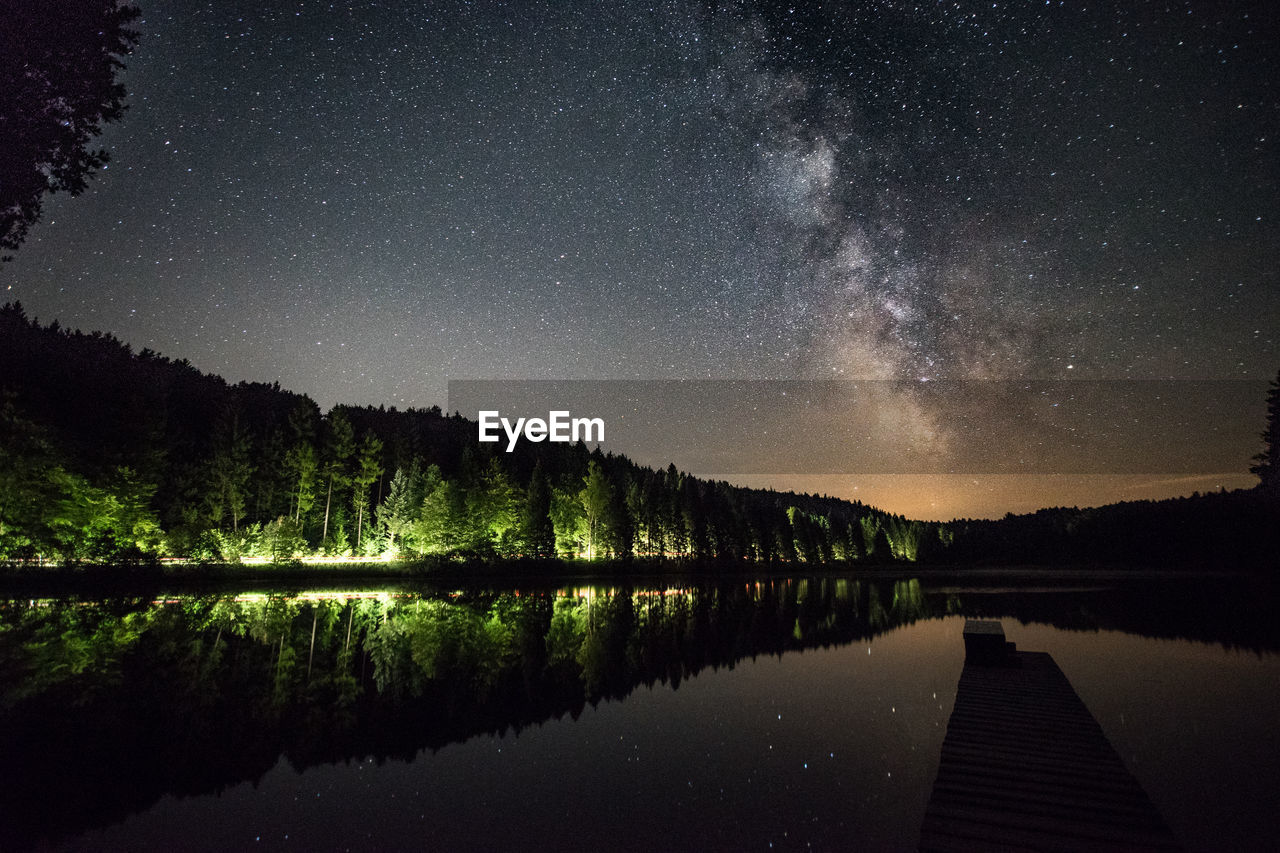 Scenic view of lake with trees reflection against star field in sky at night