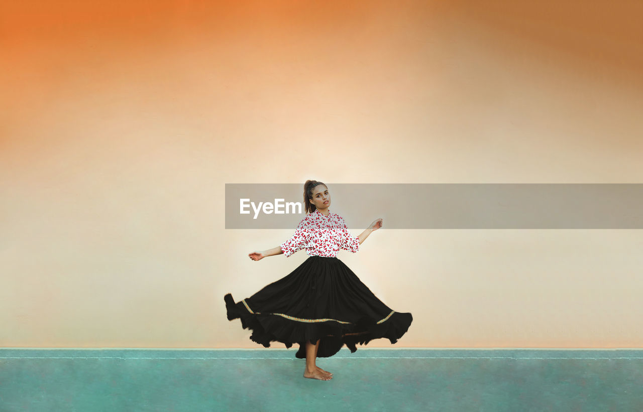 Woman wearing a skirt, dancingagainst orange wall