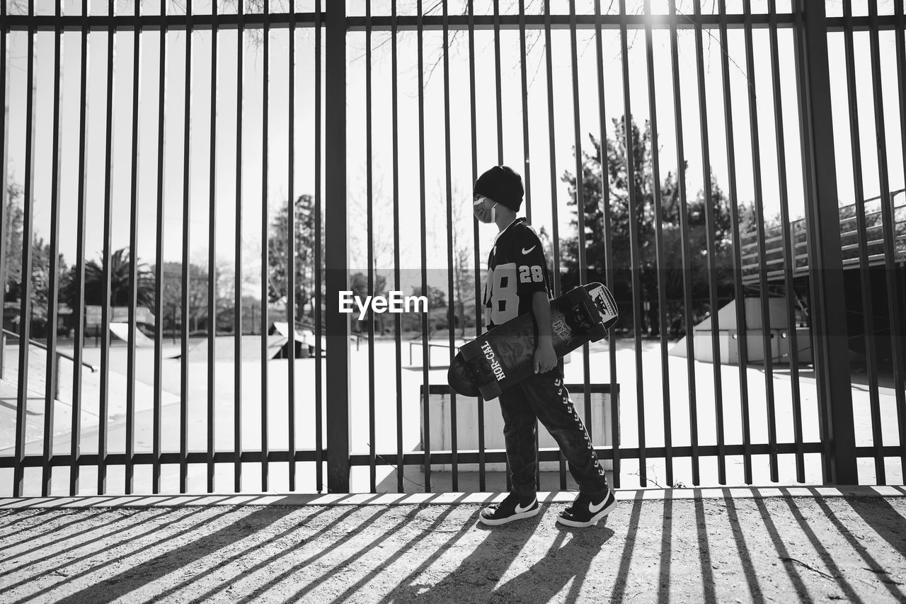 REAR VIEW OF WOMAN STANDING ON RAILING AGAINST FENCE