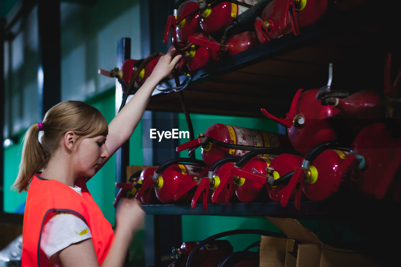 Side view of mid adult woman standing by fire extinguishers in factory