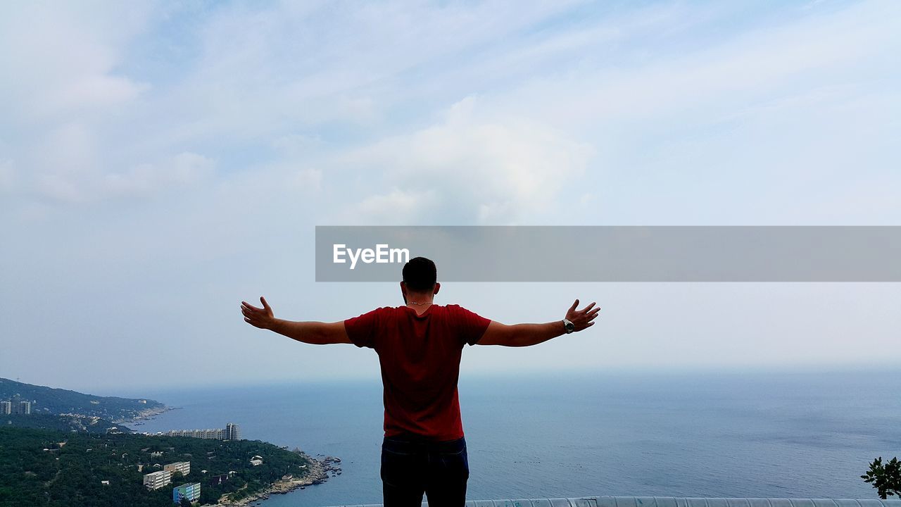 Rear view of man with arms outstretched against sky