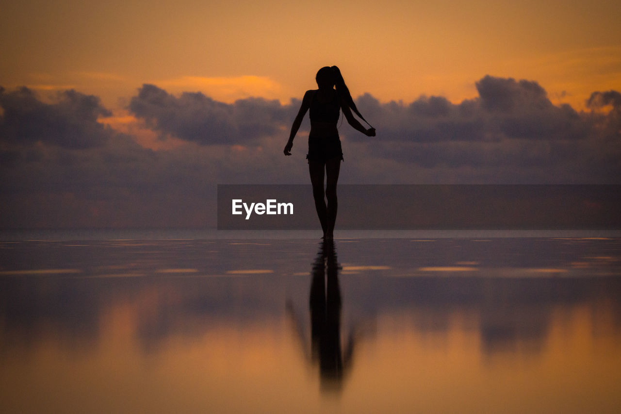 Full length of woman doing ballet dancing in infinity pool by sea against sky