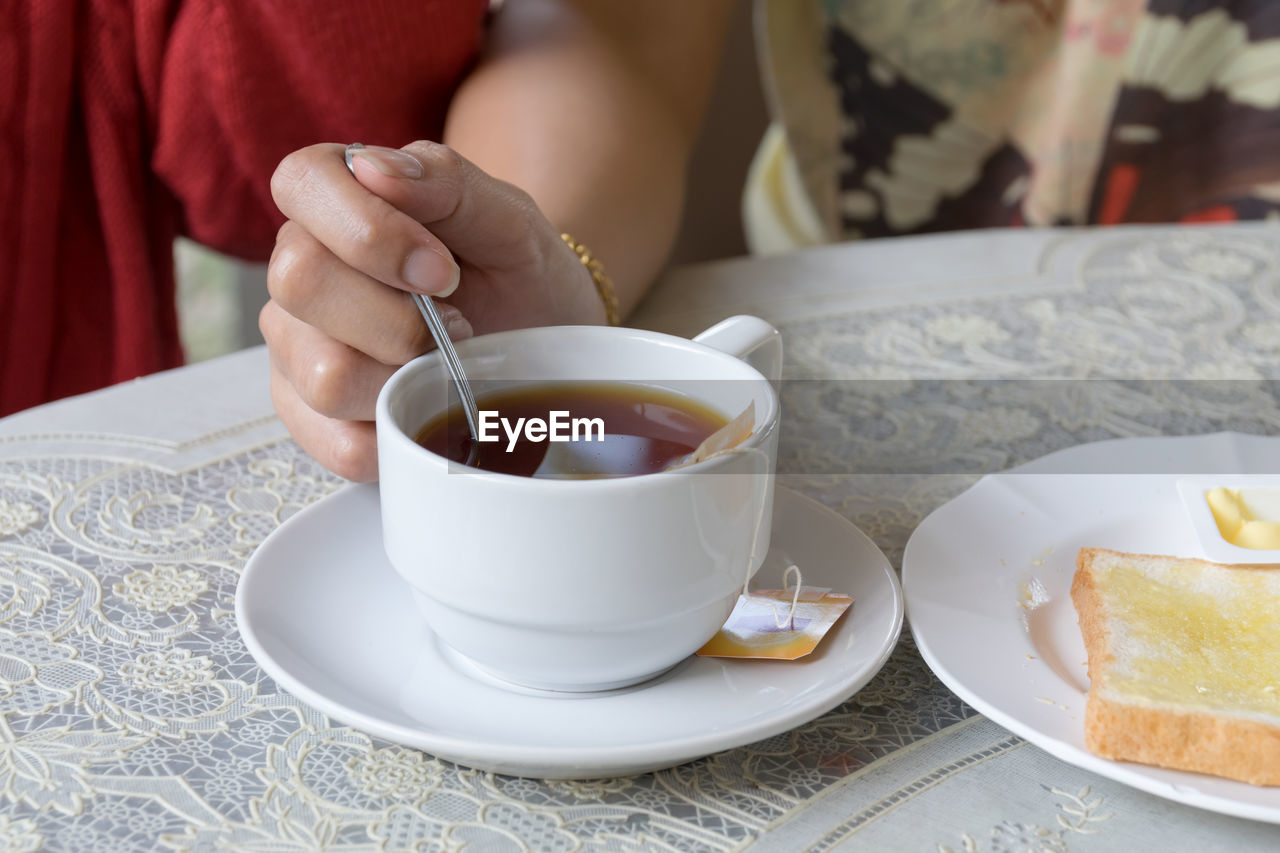 MIDSECTION OF WOMAN HOLDING COFFEE CUP AND TABLE