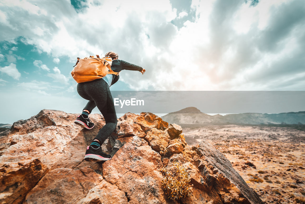 MAN STANDING ON ROCK AGAINST MOUNTAIN