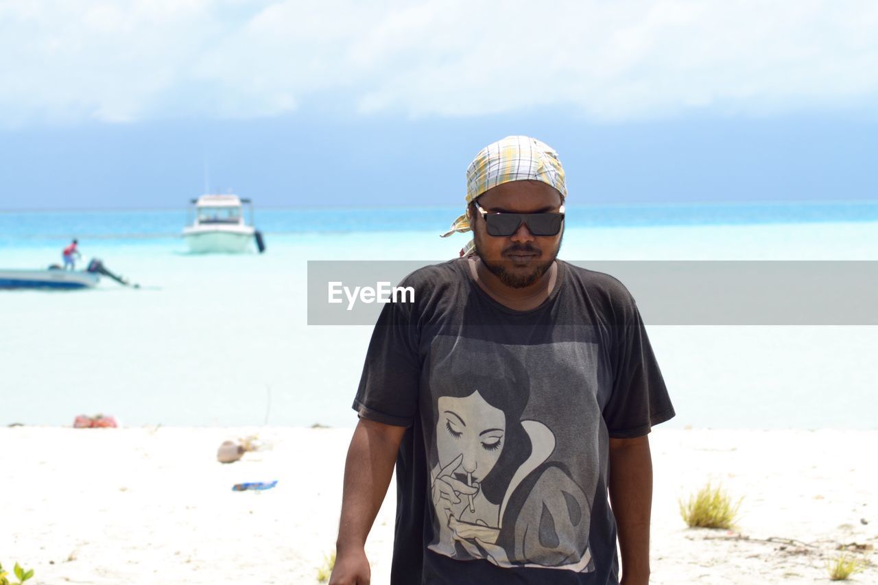 PORTRAIT OF MAN STANDING ON BEACH AGAINST SKY