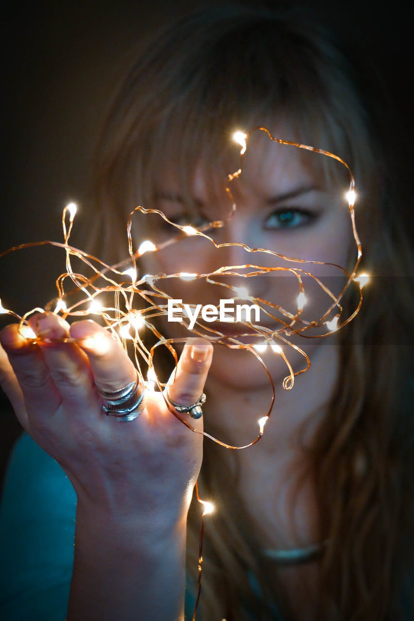 Close-up portrait of young woman holding illuminated lighting equipment