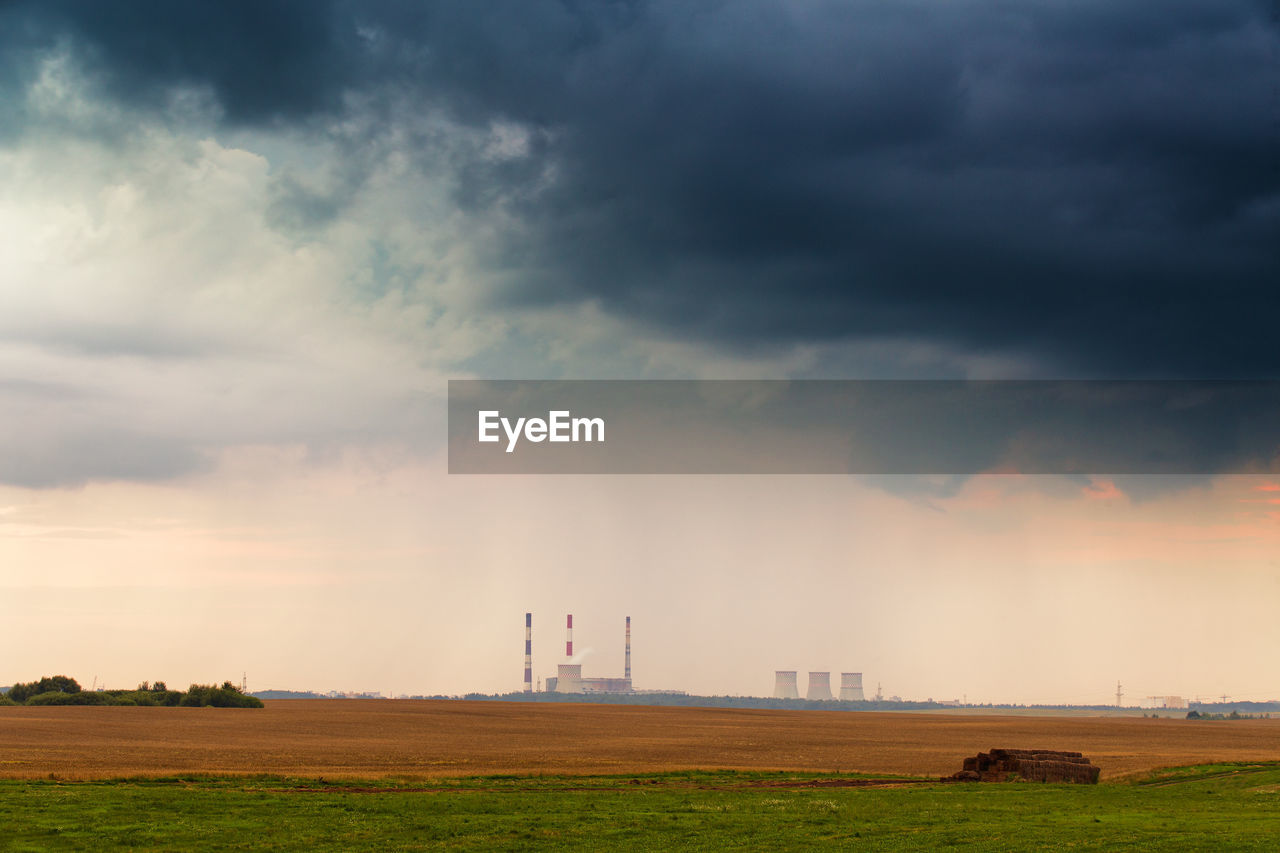 SMOKE EMITTING FROM CHIMNEY ON FIELD AGAINST CLOUDY SKY