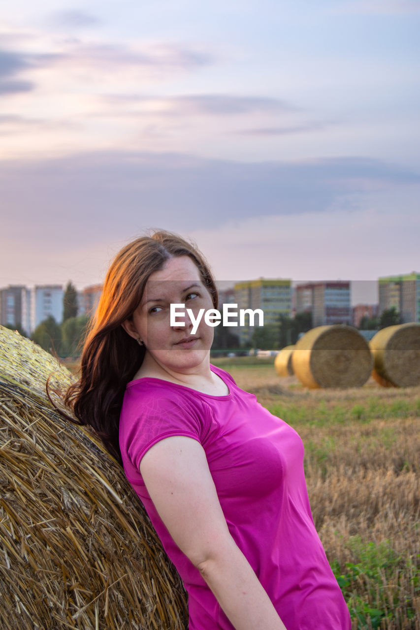 Portrait of young woman sitting on field against sky