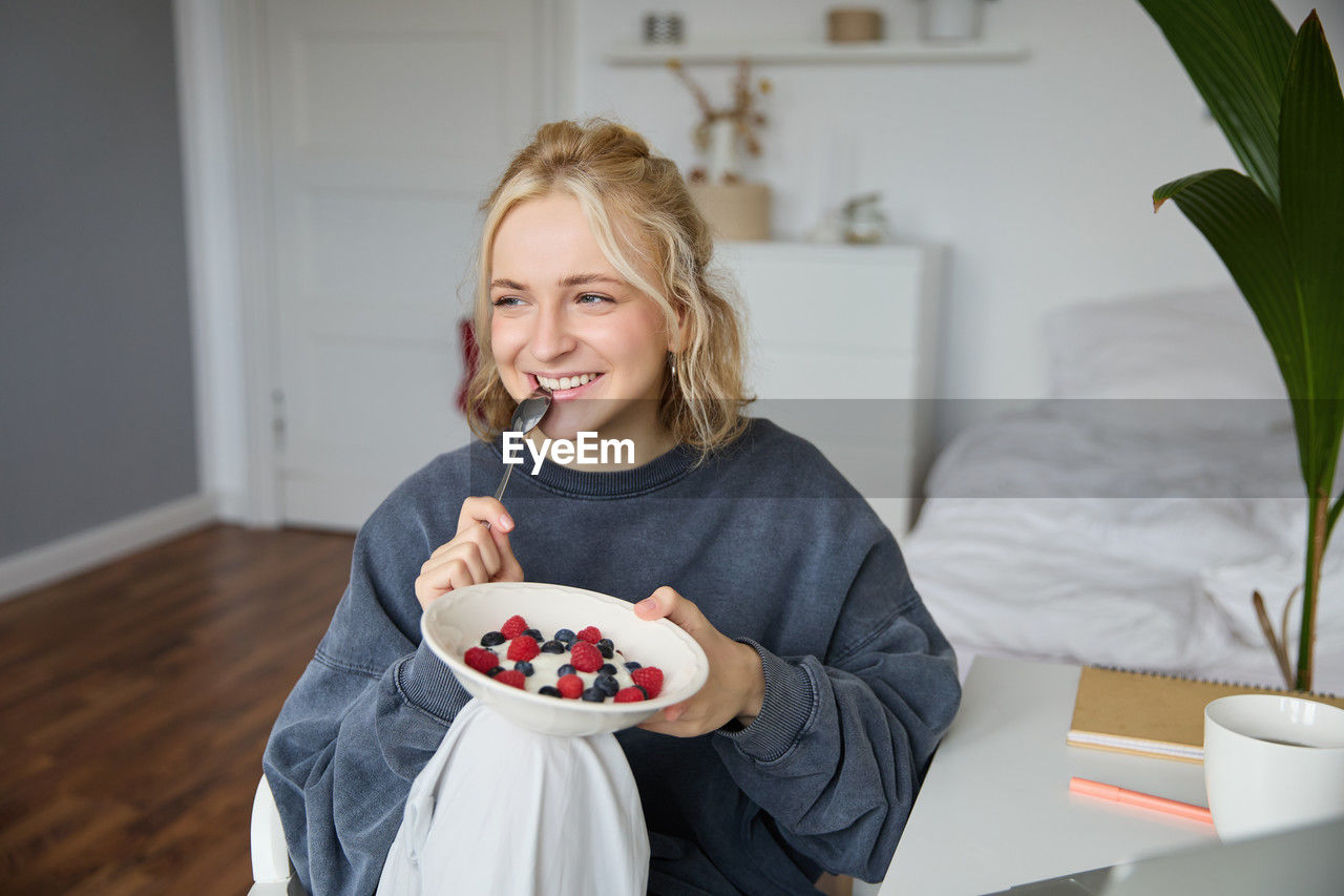 portrait of smiling young woman eating food on table at home