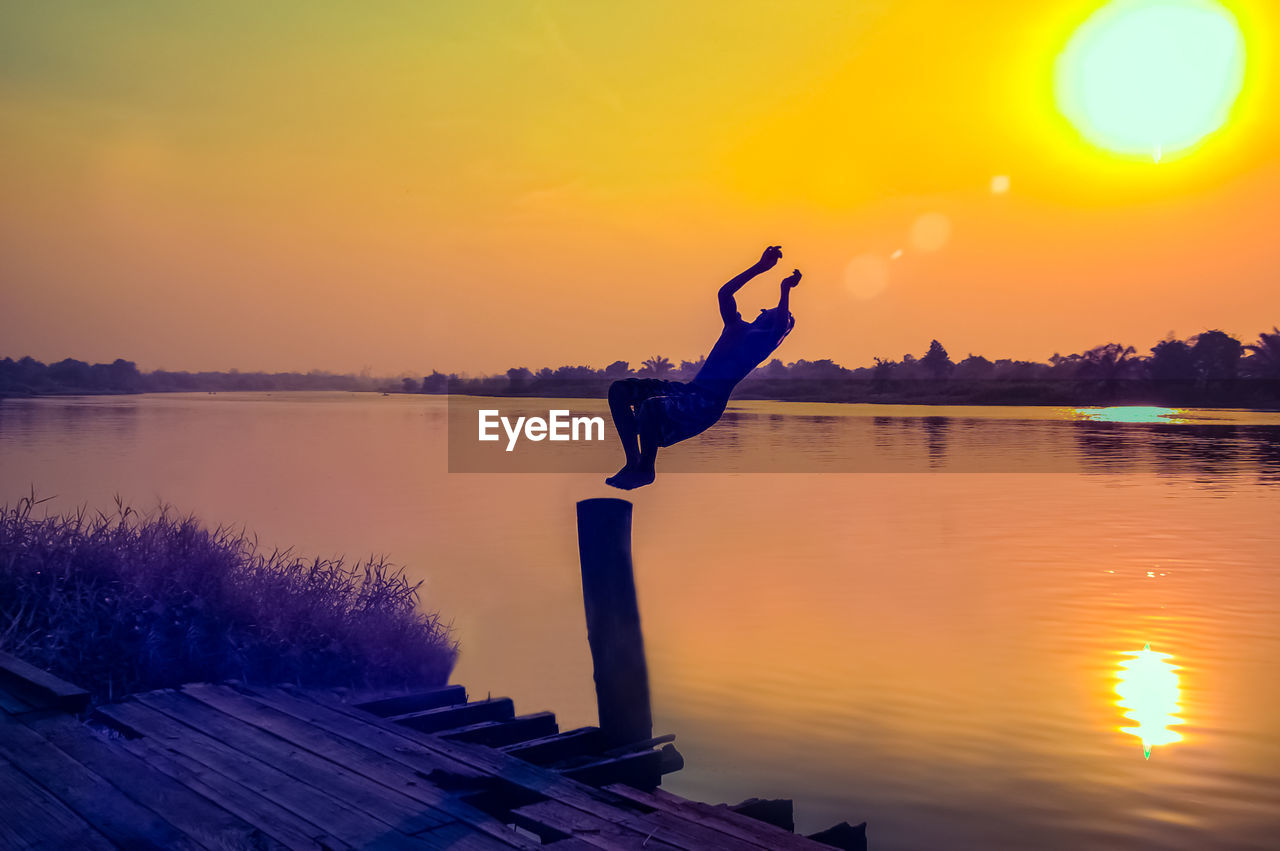 Full length of silhouette man jumping in lake against sky during sunset