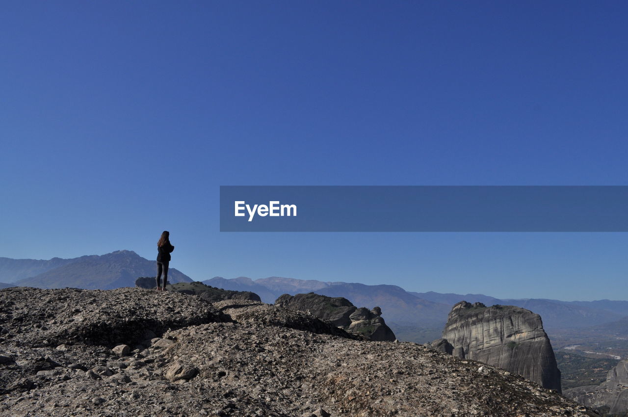 Woman standing on rocky mountains against clear blue sky