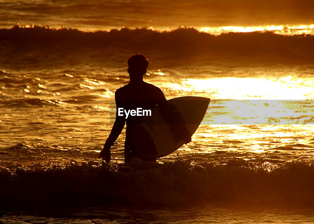 REAR VIEW OF SILHOUETTE MAN ON SEA AGAINST SKY AT SUNSET