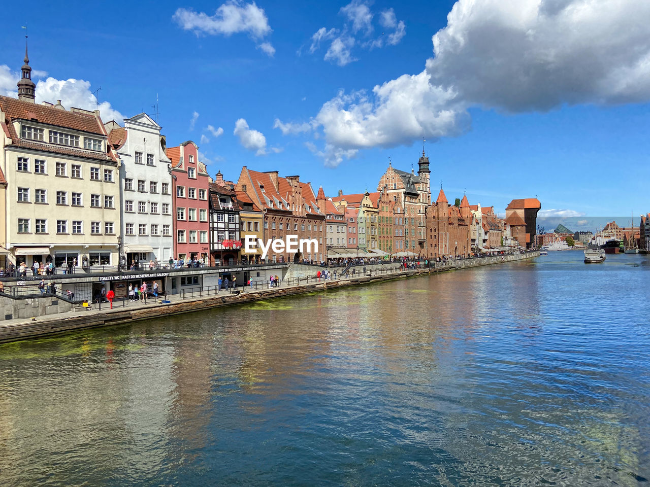 View of buildings by river against cloudy sky