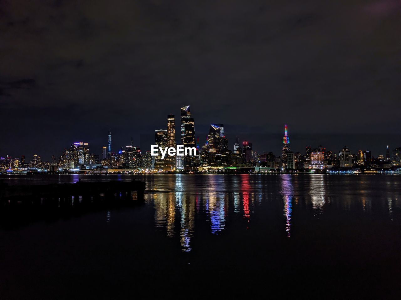 Illuminated buildings by river against sky at night