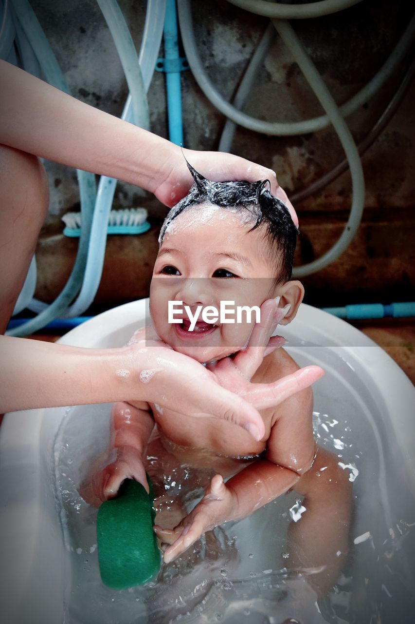 Cropped hands of mother touching baby boy taking bath in bathtub