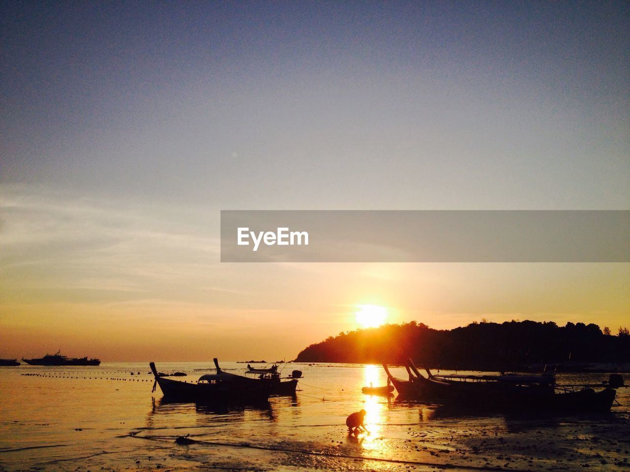 Silhouette boats moored at sea shore against sky during sunset