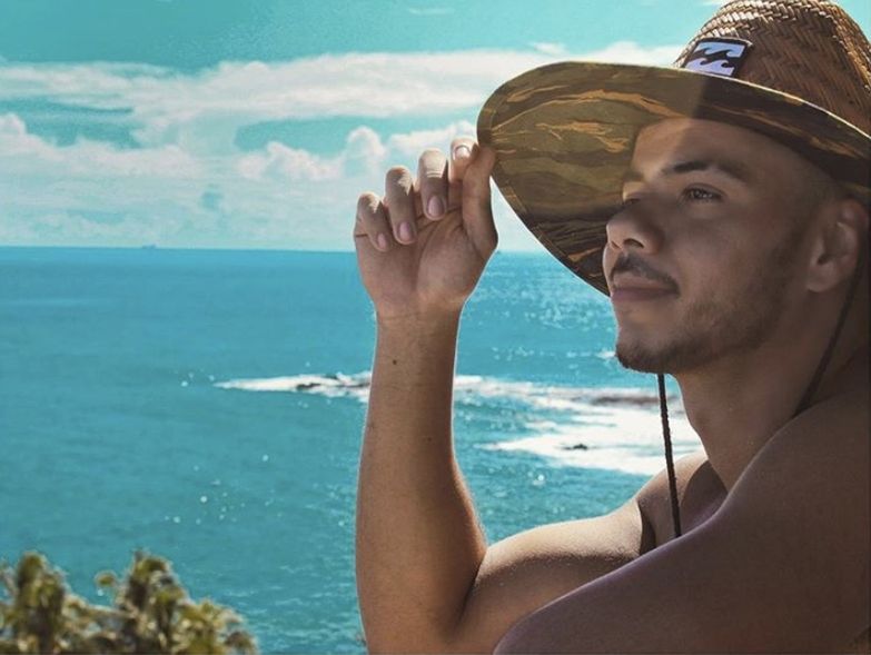 PORTRAIT OF YOUNG MAN WEARING HAT ON BEACH