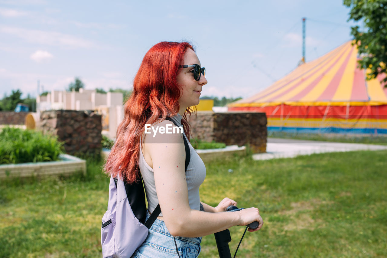 Young bright woman smiles and rides electric scooter in the summer in the city