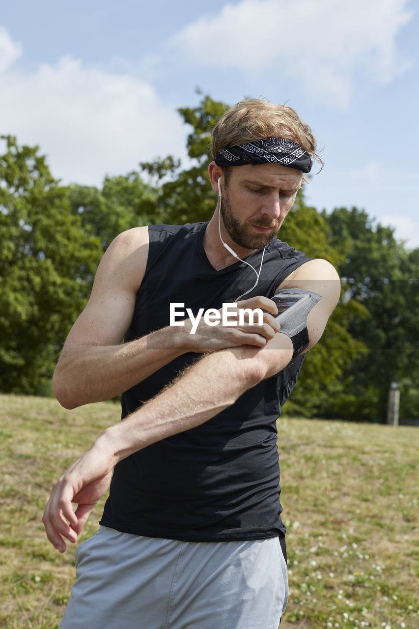 Man listening music while exercising against trees