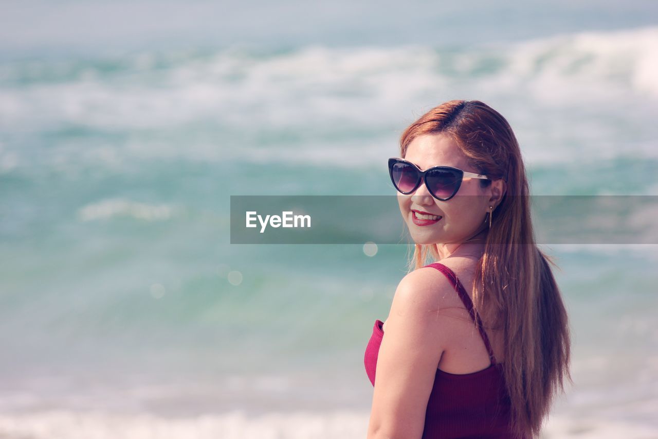 Portrait of young woman wearing sunglasses standing at beach