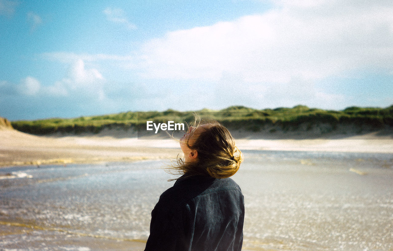 REAR VIEW OF WOMAN STANDING AT BEACH