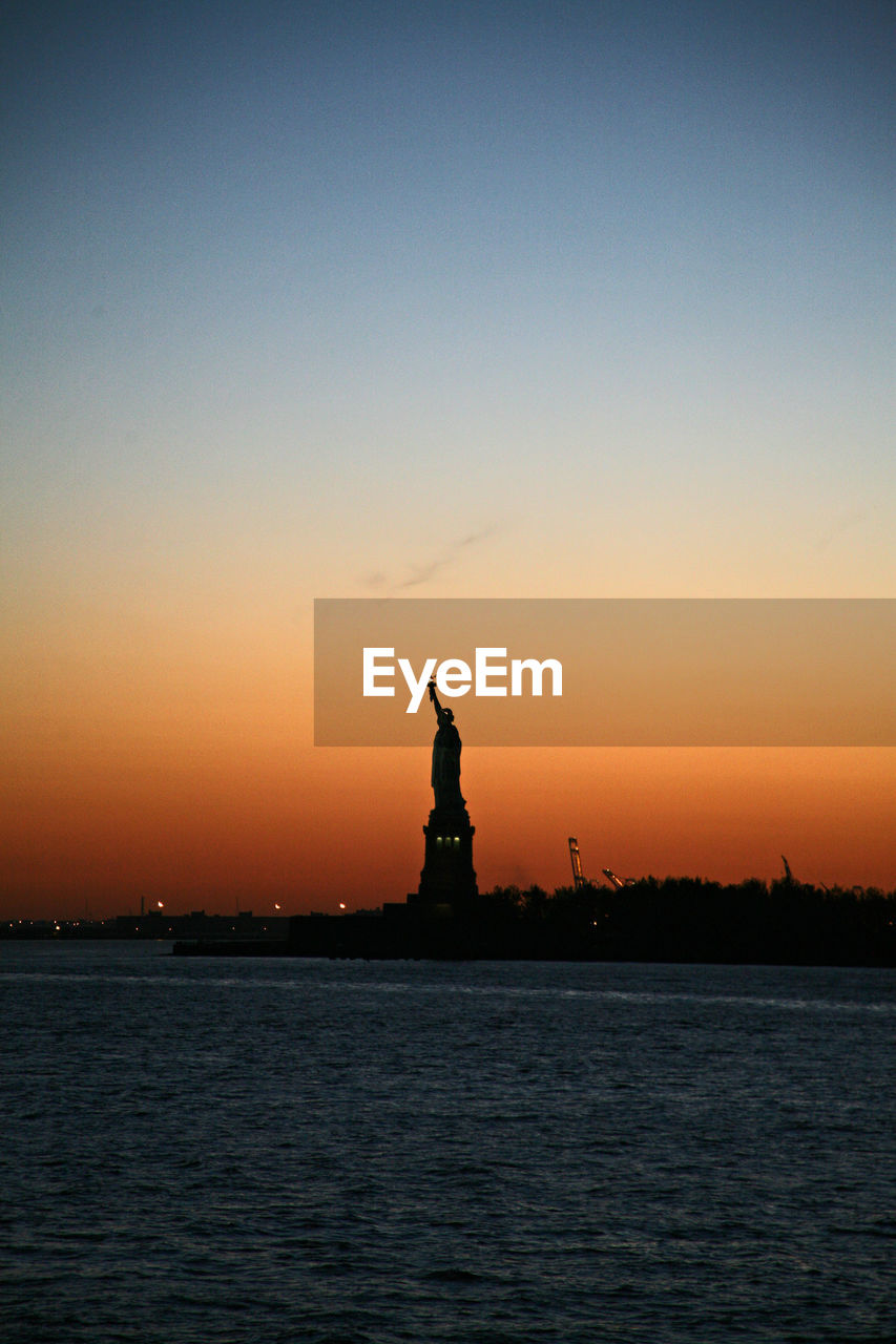 Statue of liberty by sea against sky during sunset
