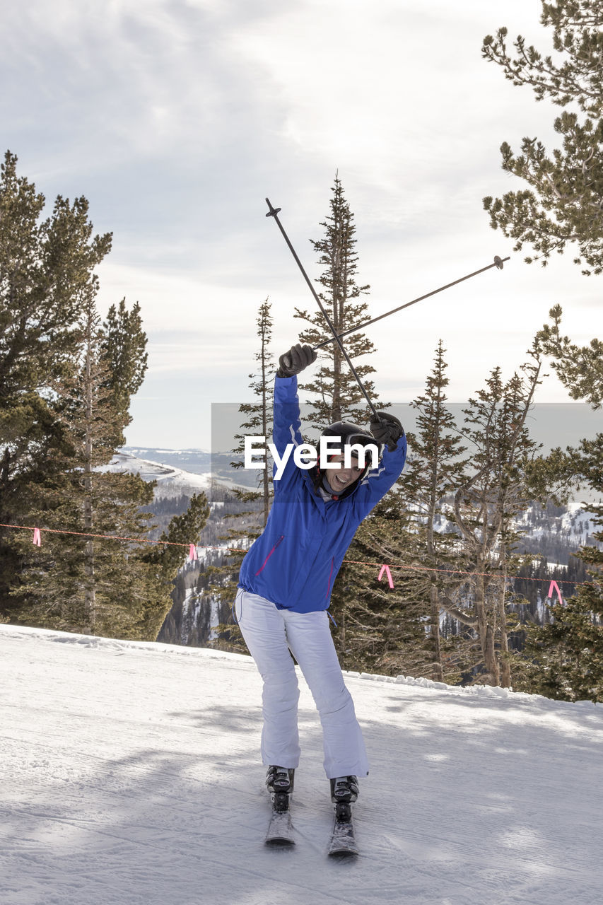Portrait of woman with arms raised skiing on snow covered land