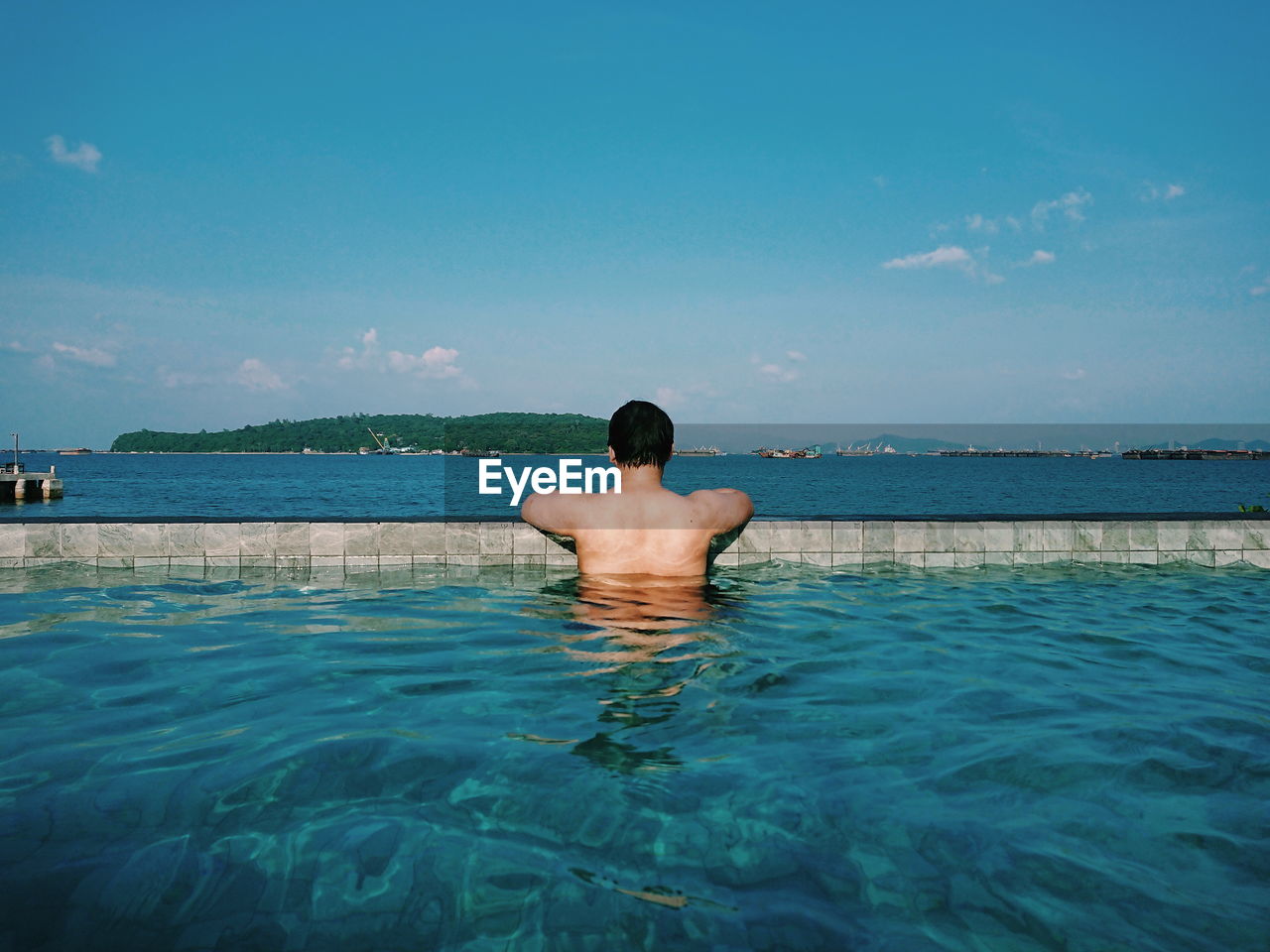 Rear view of shirtless man in infinity pool against sea