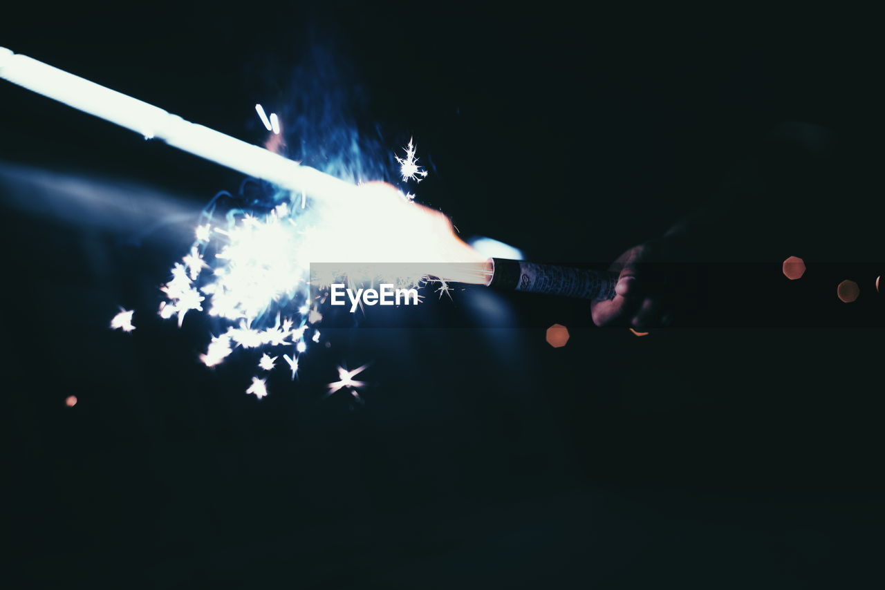 Cropped hand holding firework at night