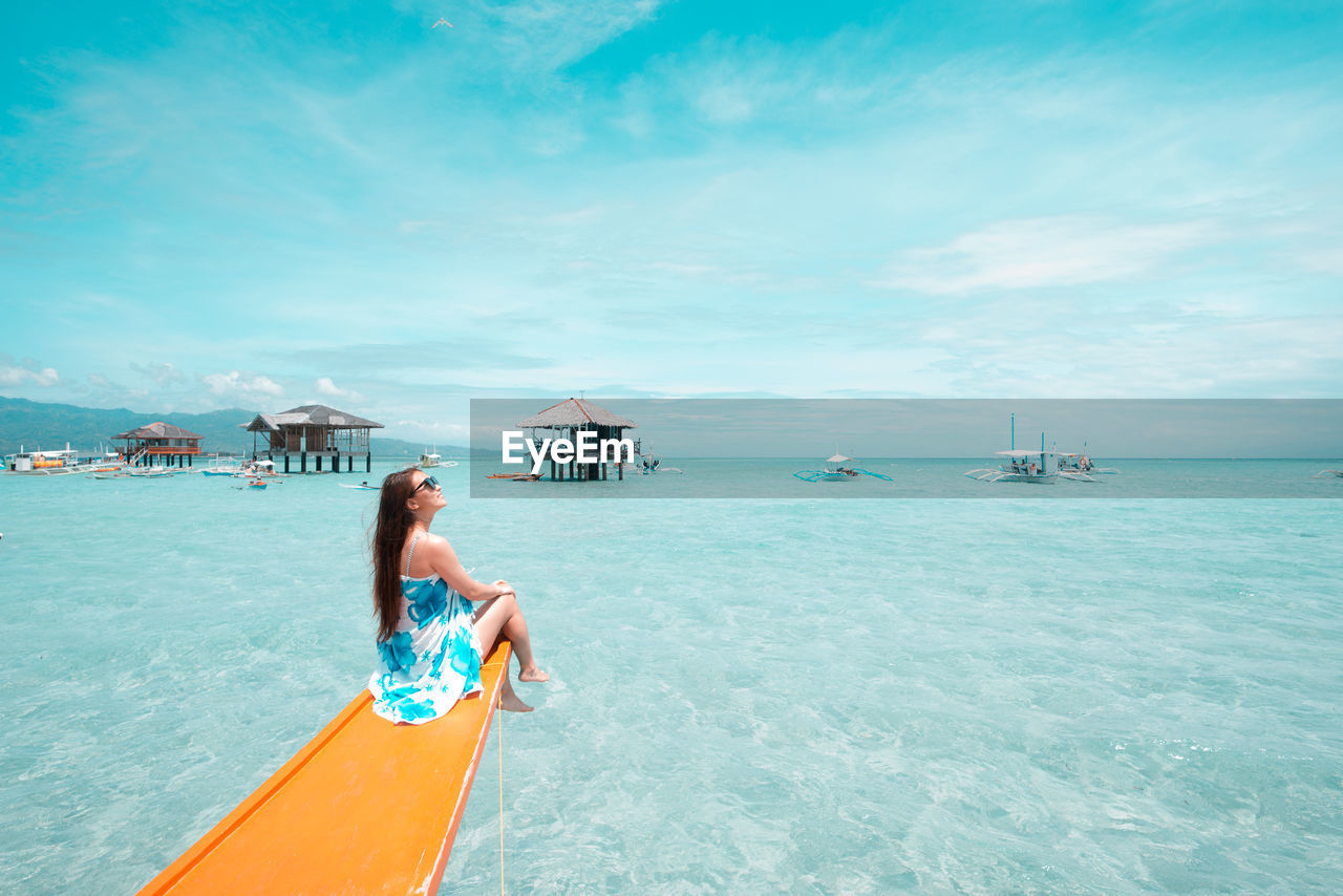 Smiling woman sitting on boat sailing in sea against cloudy sky