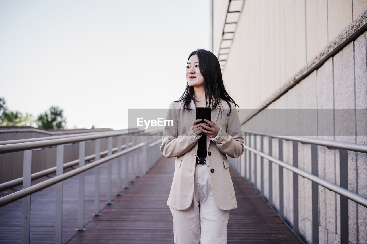 Confident beautiful chinese business woman using mobile phone in city. technology