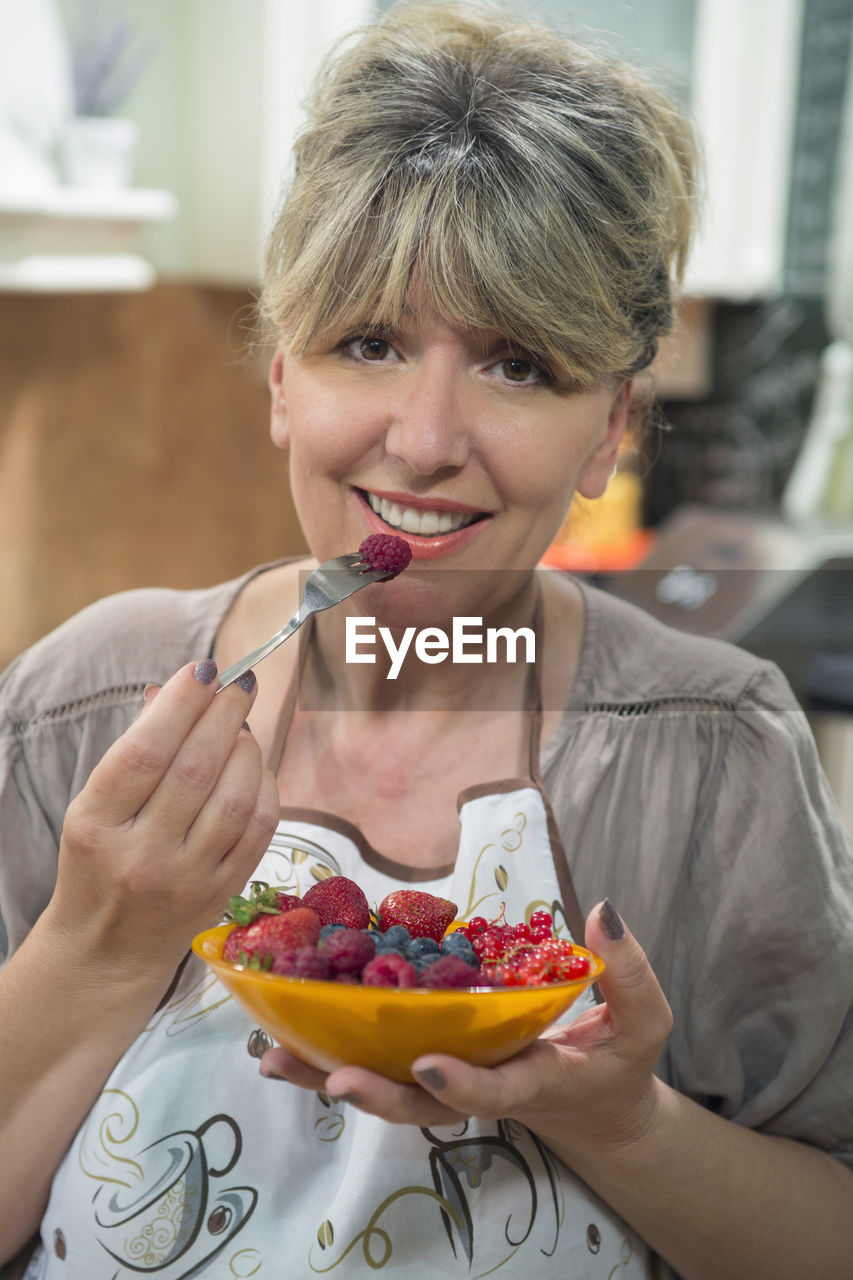 Portrait of smiling woman eating fruits at home