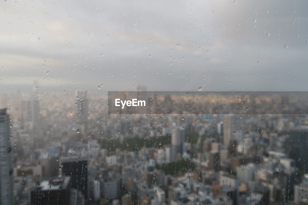 City against sky seen through wet glass window