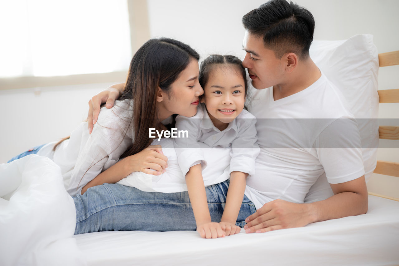 Happy loving family, father mother and child girl playing on bed