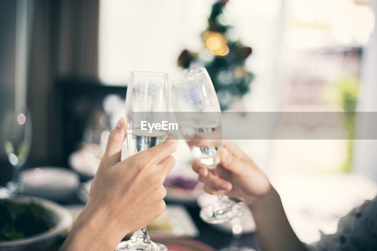 Cropped hands of female friends toasting champagne flutes at dining table