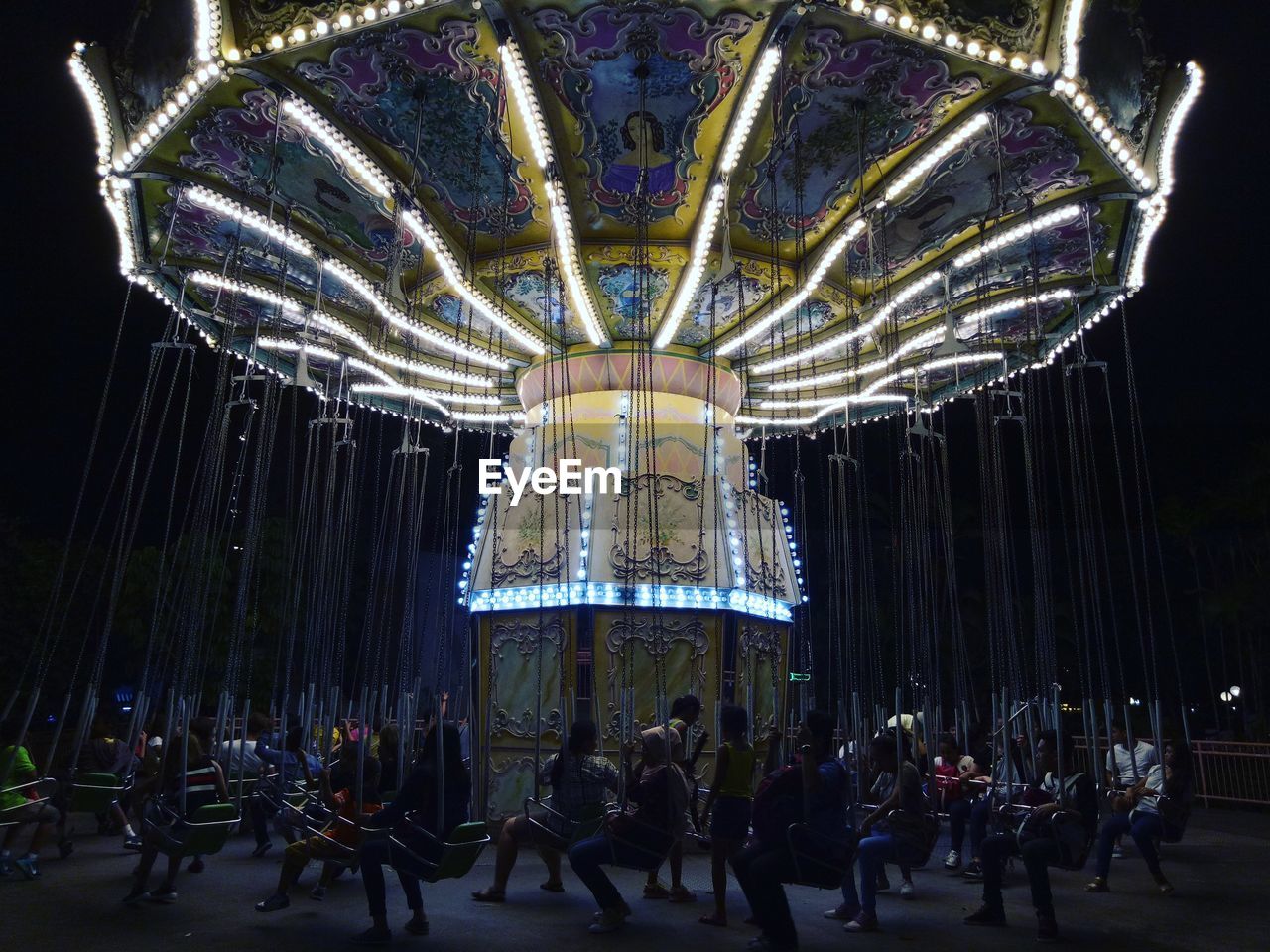 Illuminated chain swing ride in amusement park at night