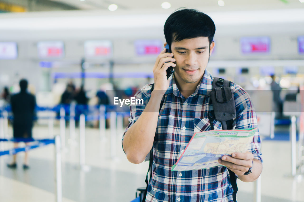 Young man talking on phone while holding map at airport