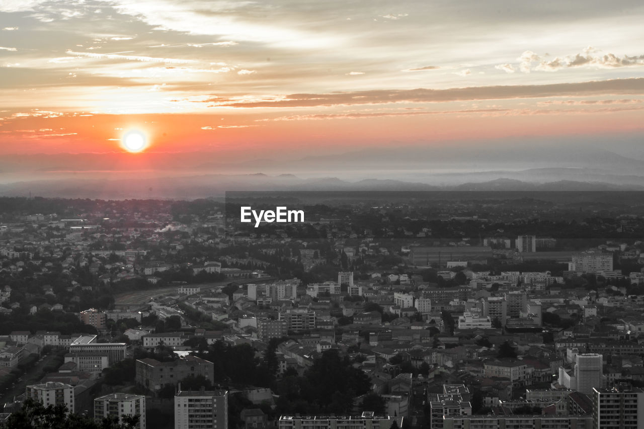 HIGH ANGLE VIEW OF ILLUMINATED CITYSCAPE AGAINST SKY DURING SUNSET