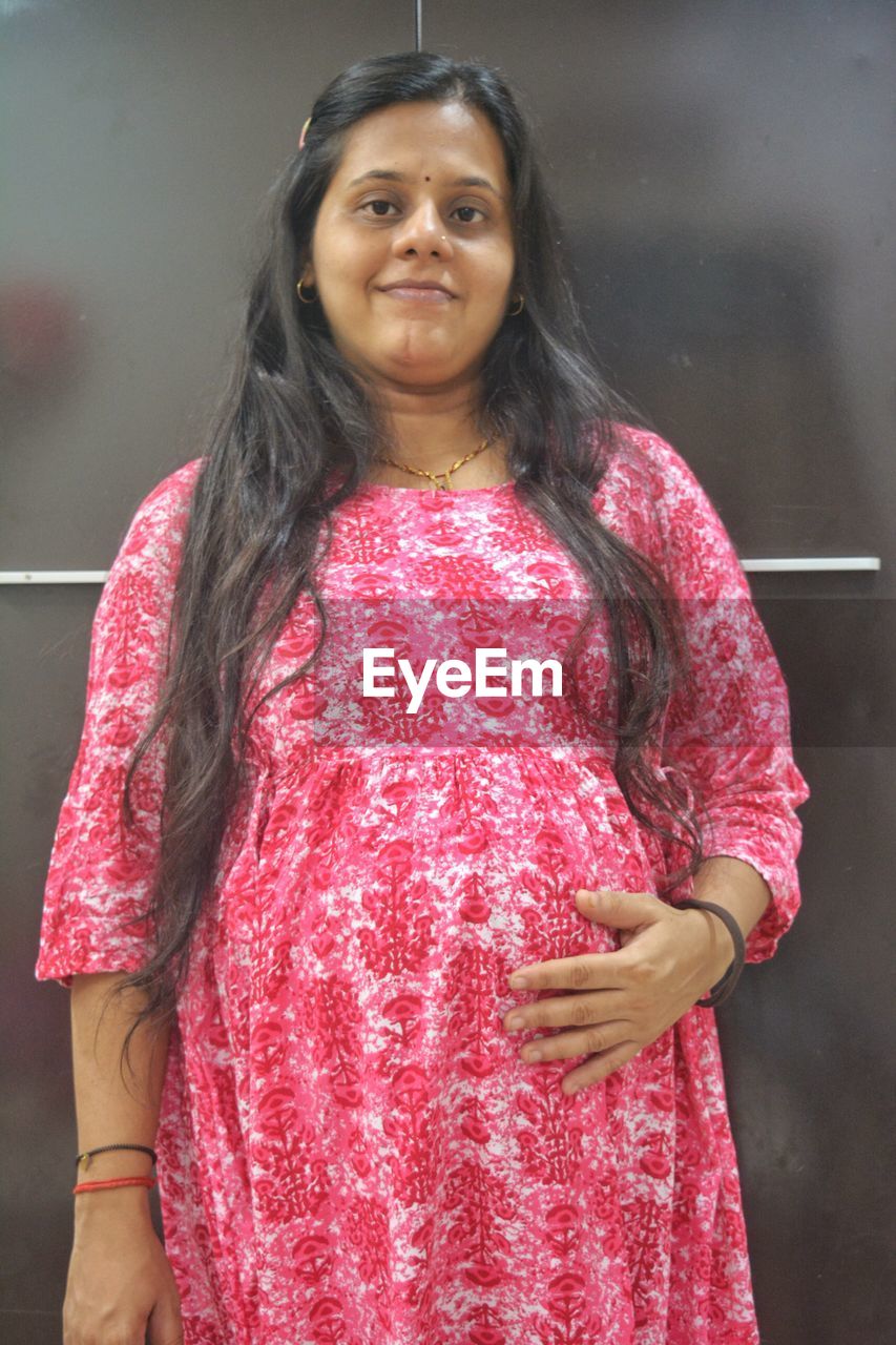 looking at camera, portrait, one person, smiling, pink, women, standing, adult, happiness, emotion, clothing, waist up, sari, red, front view, long hair, three quarter length, indoors, dress, black hair, traditional clothing, hairstyle, fashion, photo shoot, female, cheerful, person, young adult, lifestyles