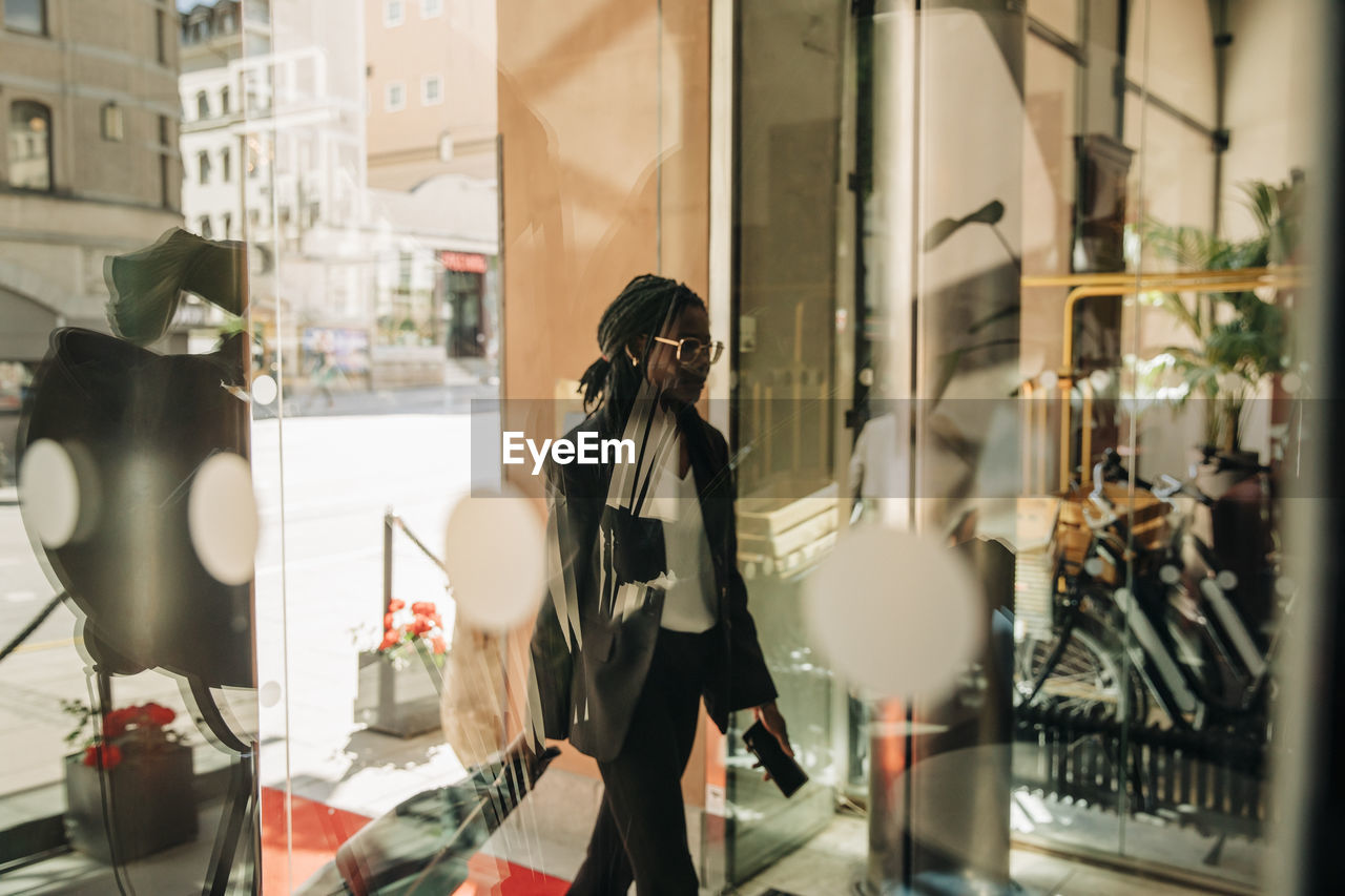 Businesswoman with suitcase arriving in hotel seen through glass