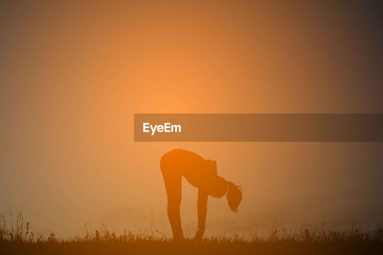 Silhouette woman practicing yoga on field against sky during sunset