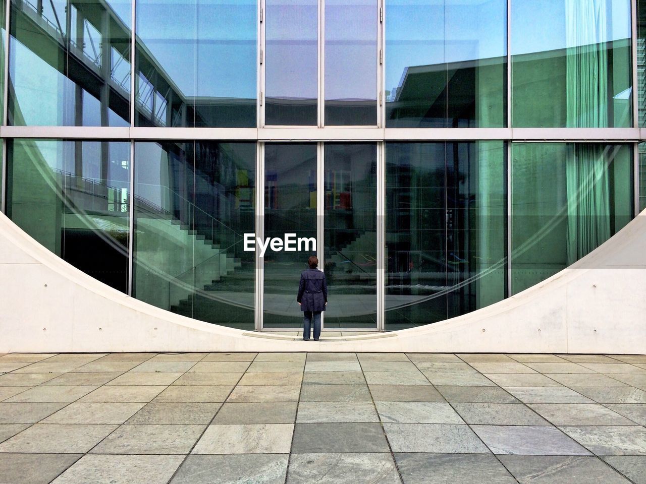 Full length rear view of woman standing in front of glass building
