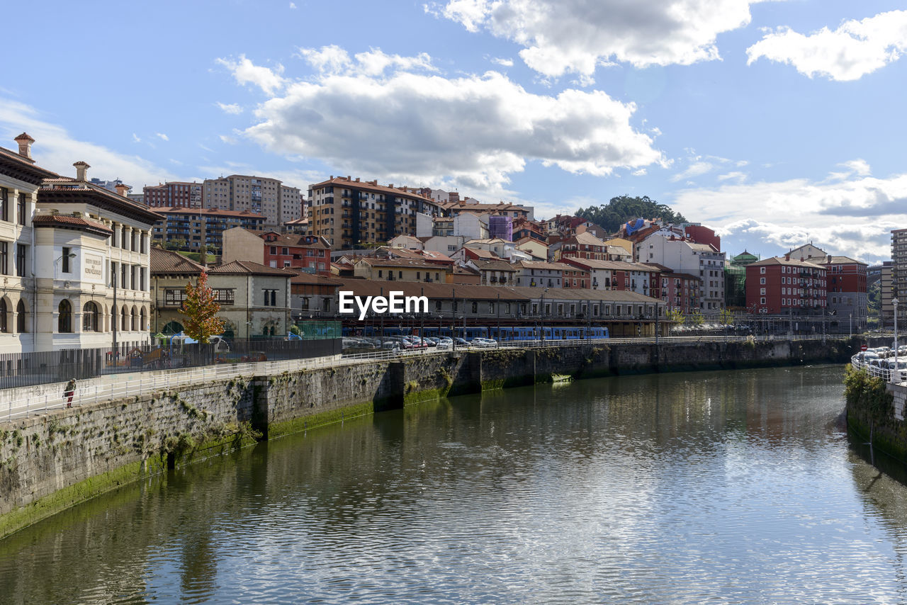 BRIDGE OVER RIVER BY BUILDINGS AGAINST SKY