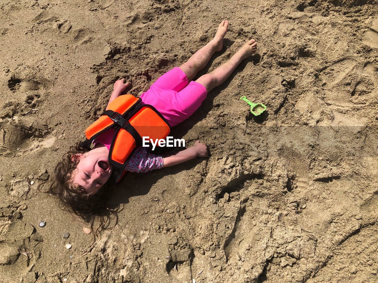 Portrait of boy in life jacket crying while lying at beach